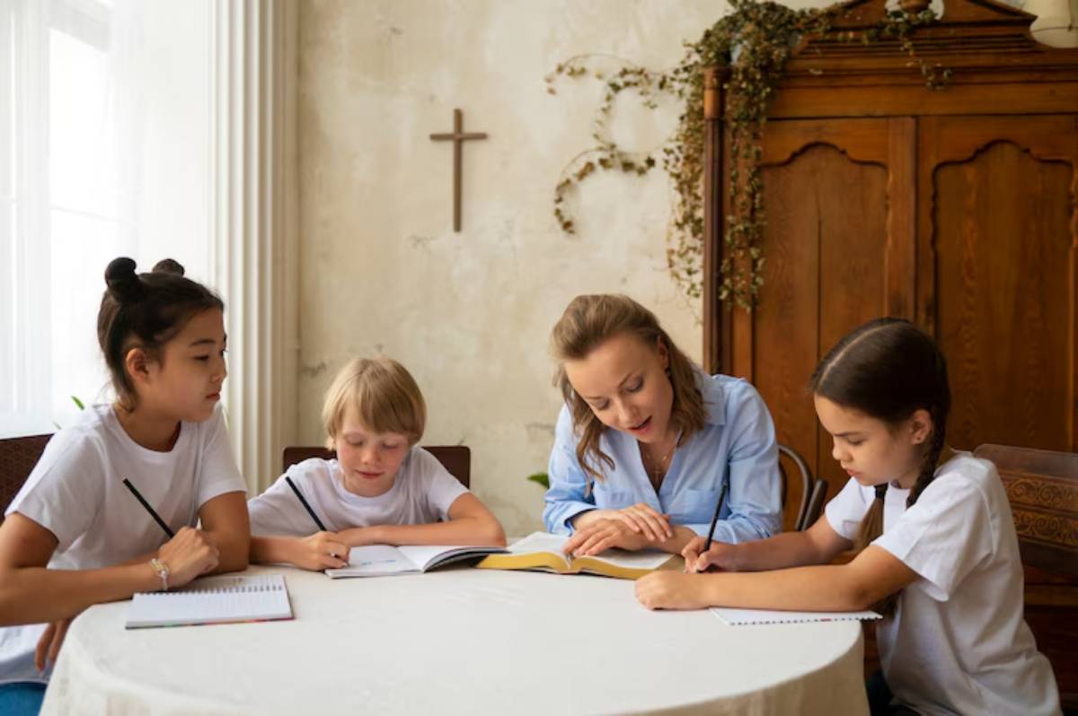 A group of children and an adult gather around a table, engaged in study, with books and notebooks spread out.