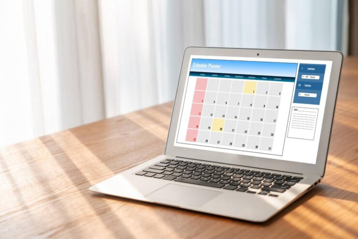 Laptop displaying a digital calendar planner with highlighted dates, placed on a wooden table under soft sunlight.