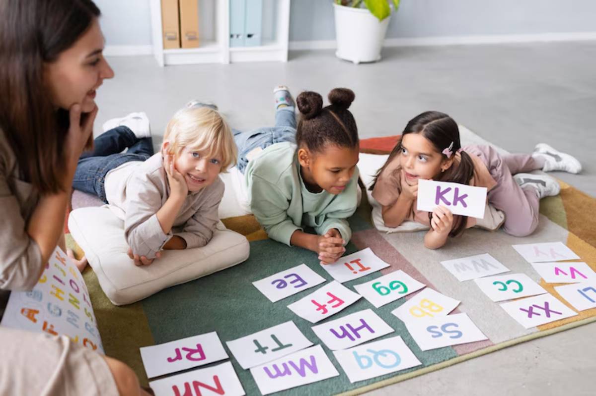 A group of young children and a teacher engaging in a playful learning activity on the floor, using colorful alphabet flashcards to practice letter recognition in a bright and friendly classroom setting.