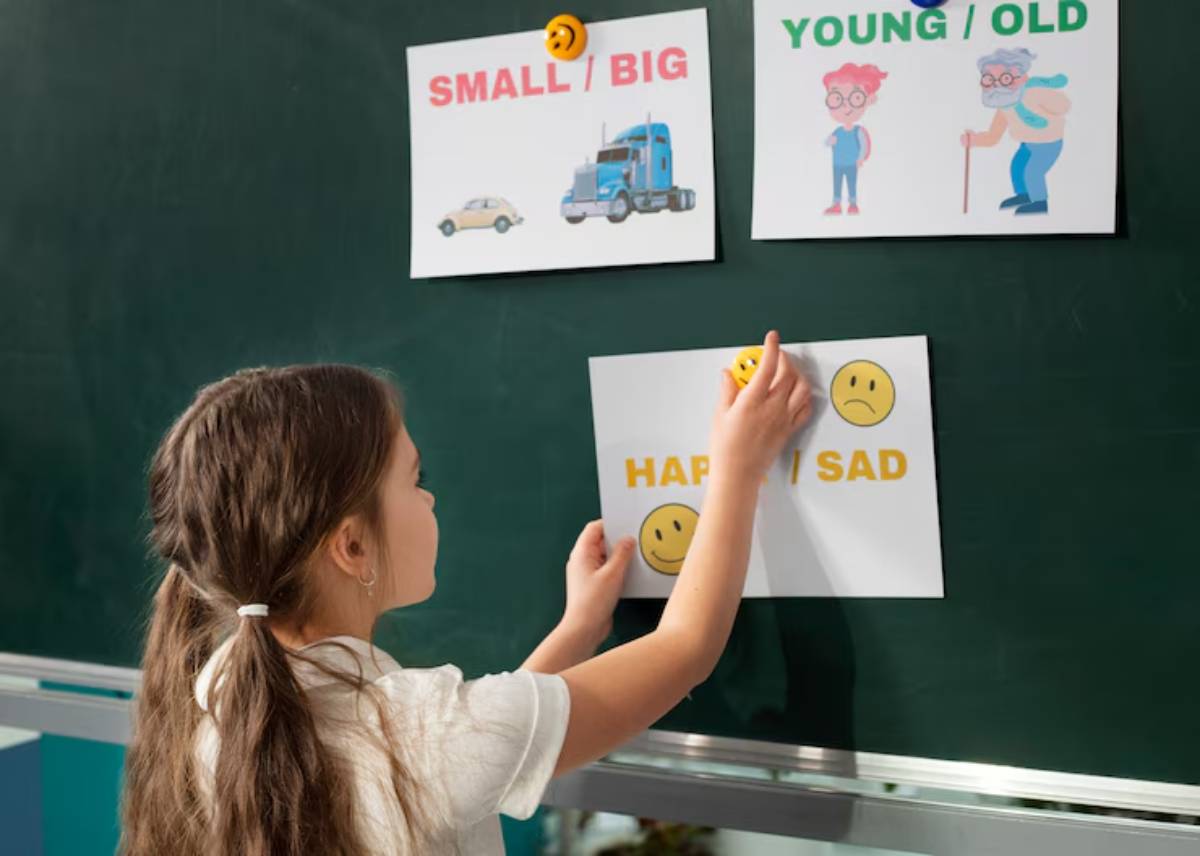 A child arranges emotion cards on a classroom board, depicting happy/sad, alongside categories of small/big and young/old.