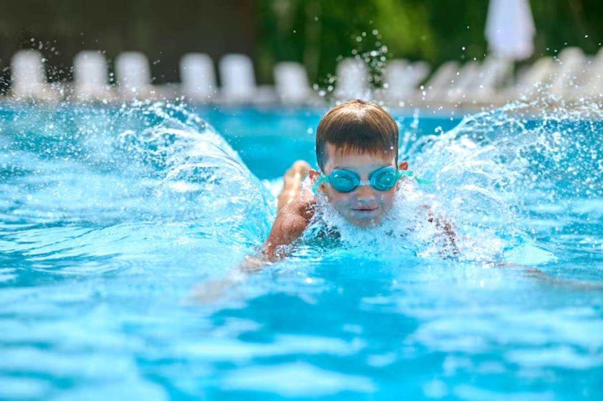 A child swims energetically in a bright blue pool, creating splashes of water. Sunlight reflects off the surface, enhancing the vibrant scene.