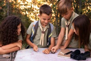 A group of children in scouting attire gather around a map, examining compasses and planning their outdoor adventure.