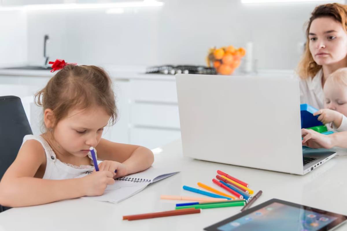 A girl is drawing in a notebook at a kitchen table, surrounded by colorful markers and a laptop, with oranges in the background.