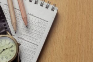 A wooden desk features an open calendar, two colored pencils, and a vintage watch, suggesting planning and organization.