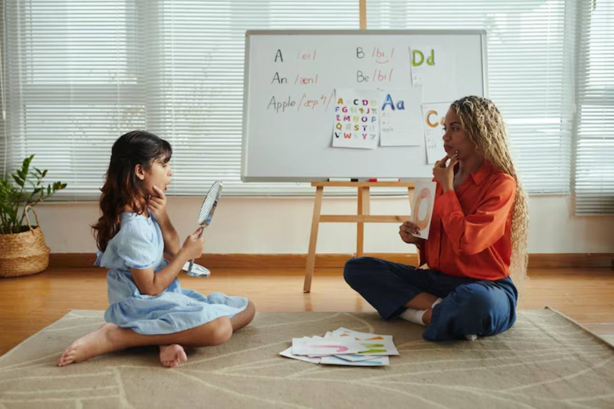 A child and adult sit on the floor, engaging in an educational activity, with a whiteboard displaying letters and colorful worksheets.