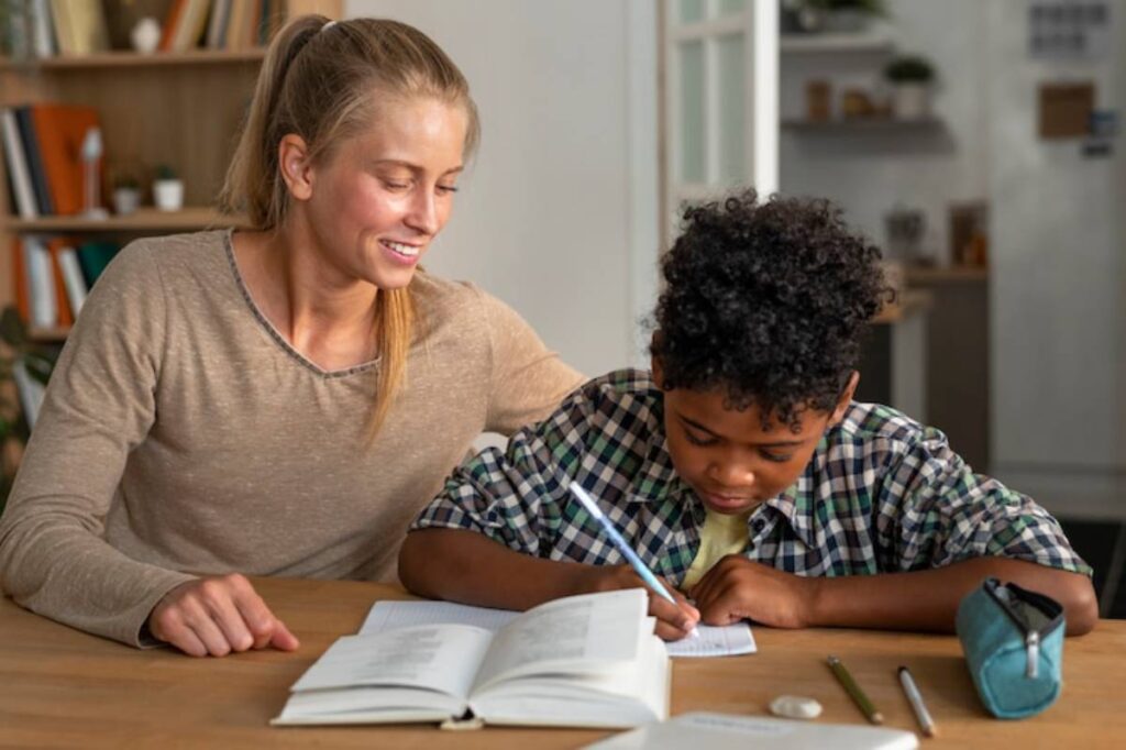 A woman supports a child with homework at a wooden table, surrounded by books and stationery in a cozy, well-lit room.