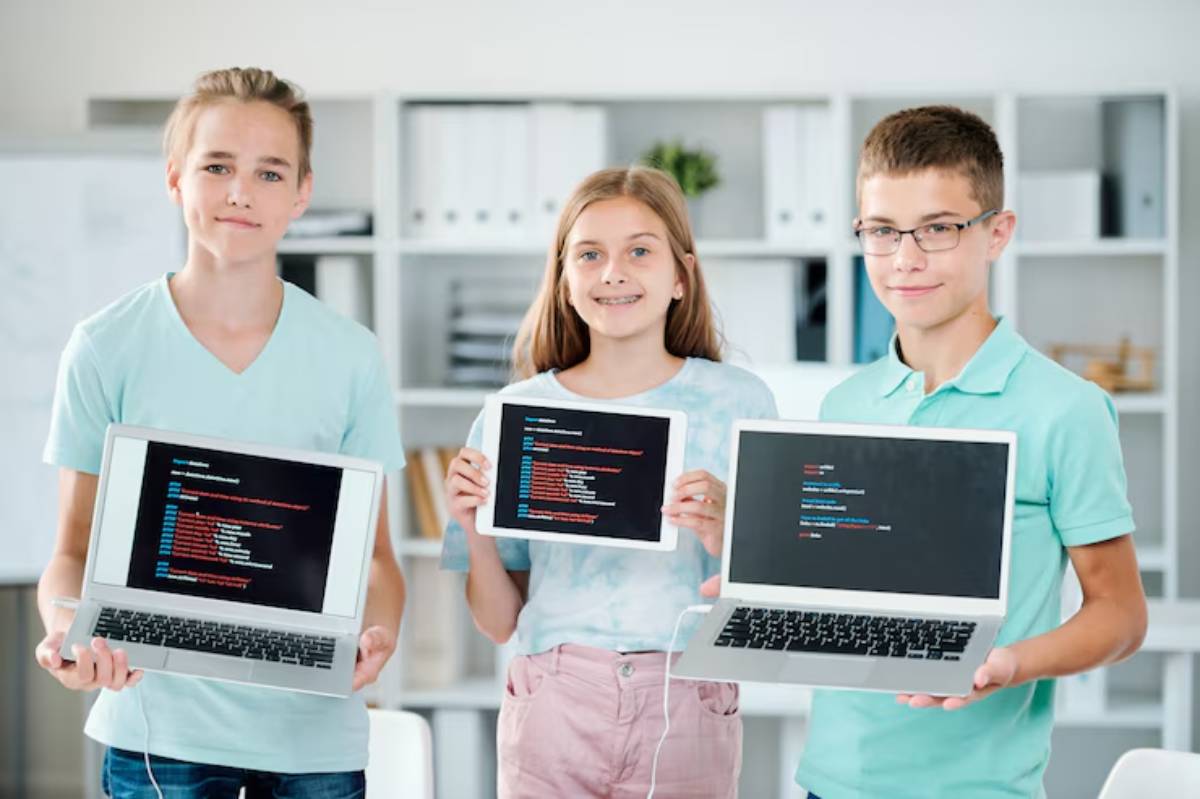 Three young individuals hold laptops displaying code on their screens, set in a modern office environment with shelves in the background.