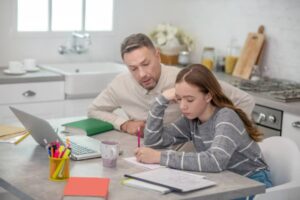 A child working independently at a desk while a parent sips coffee nearby, relaxed