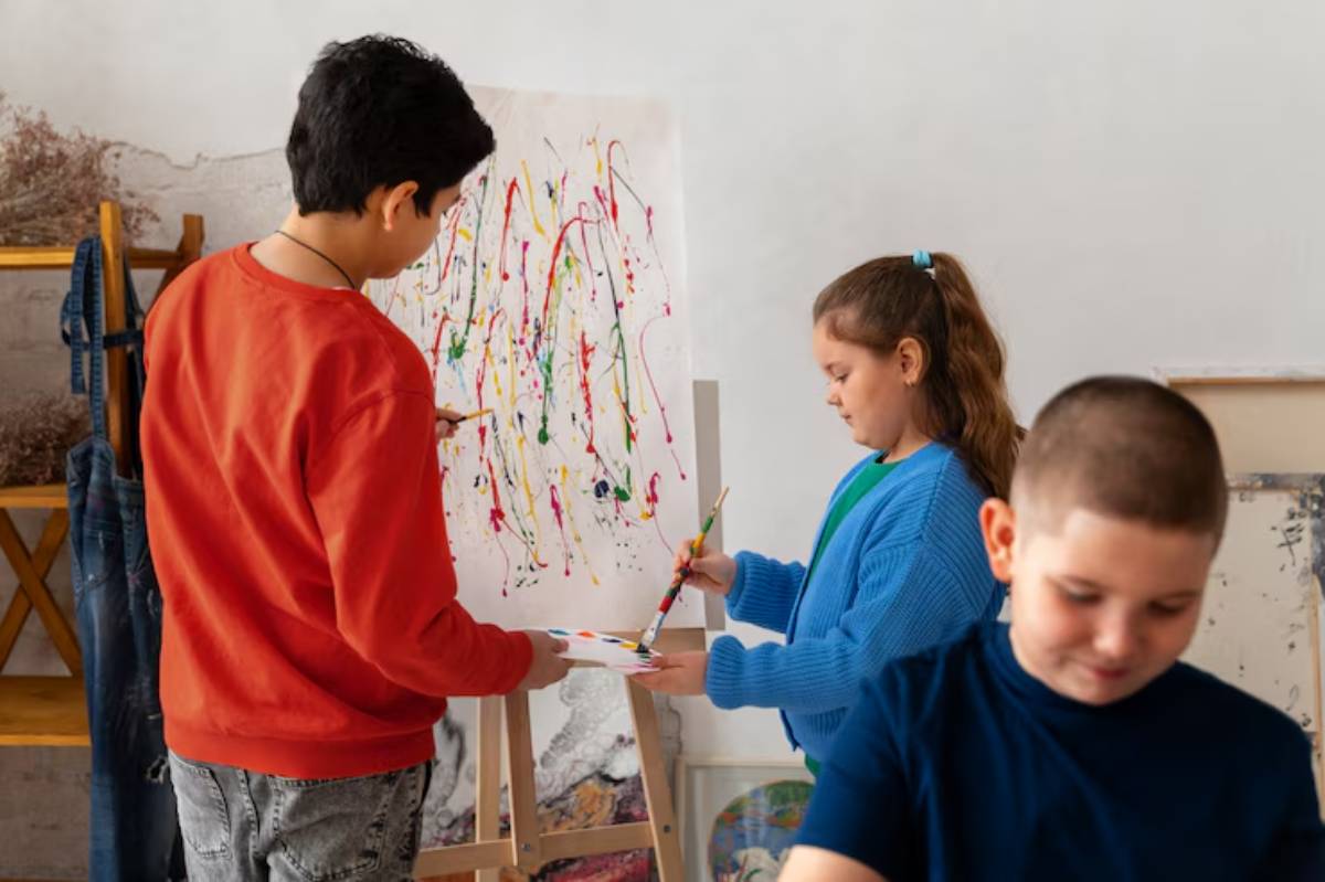Children engaged in painting at an easel, surrounded by colorful splashes of paint on the canvas in a creative studio setting.