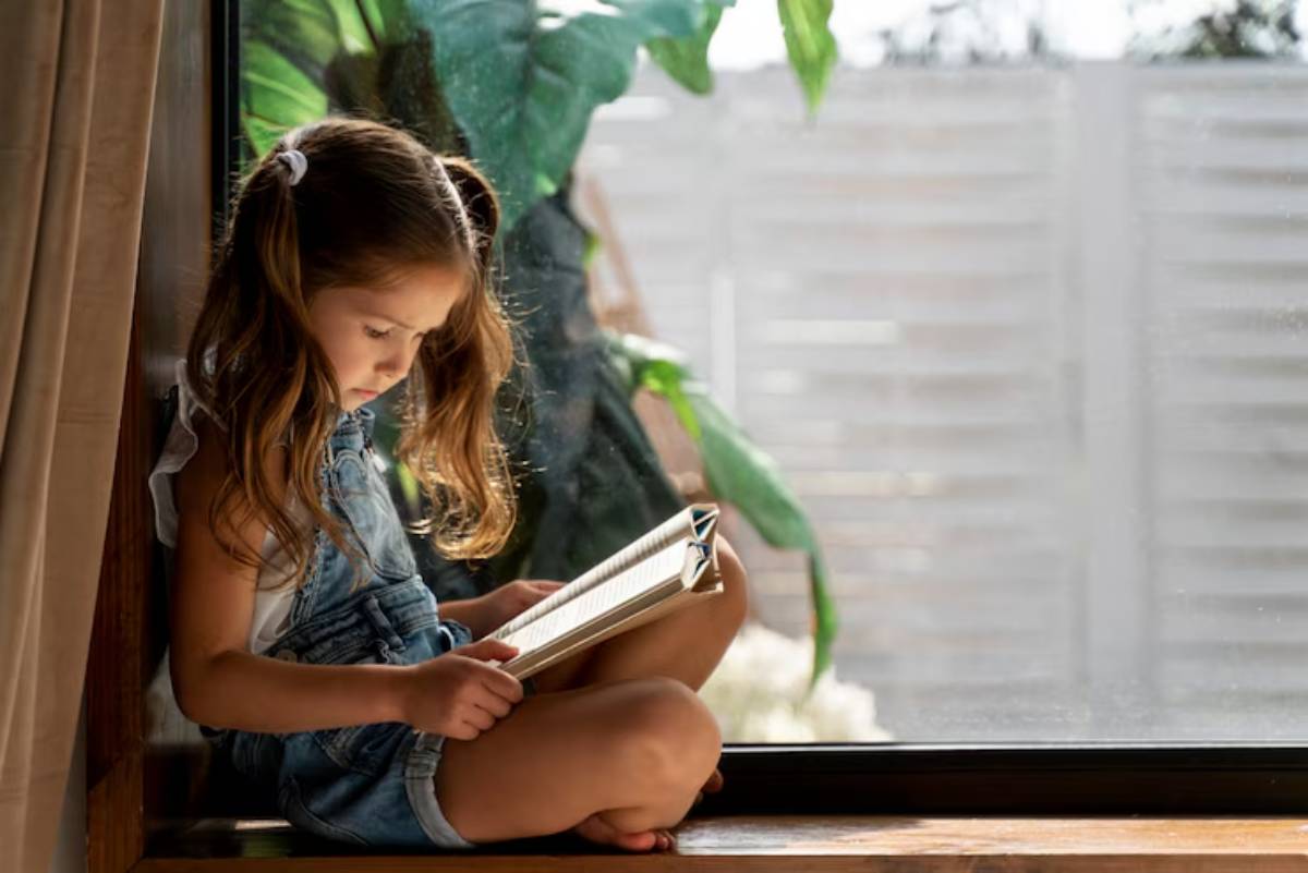 A child sits cross-legged on a windowsill, reading a book, surrounded by greenery and soft natural light.