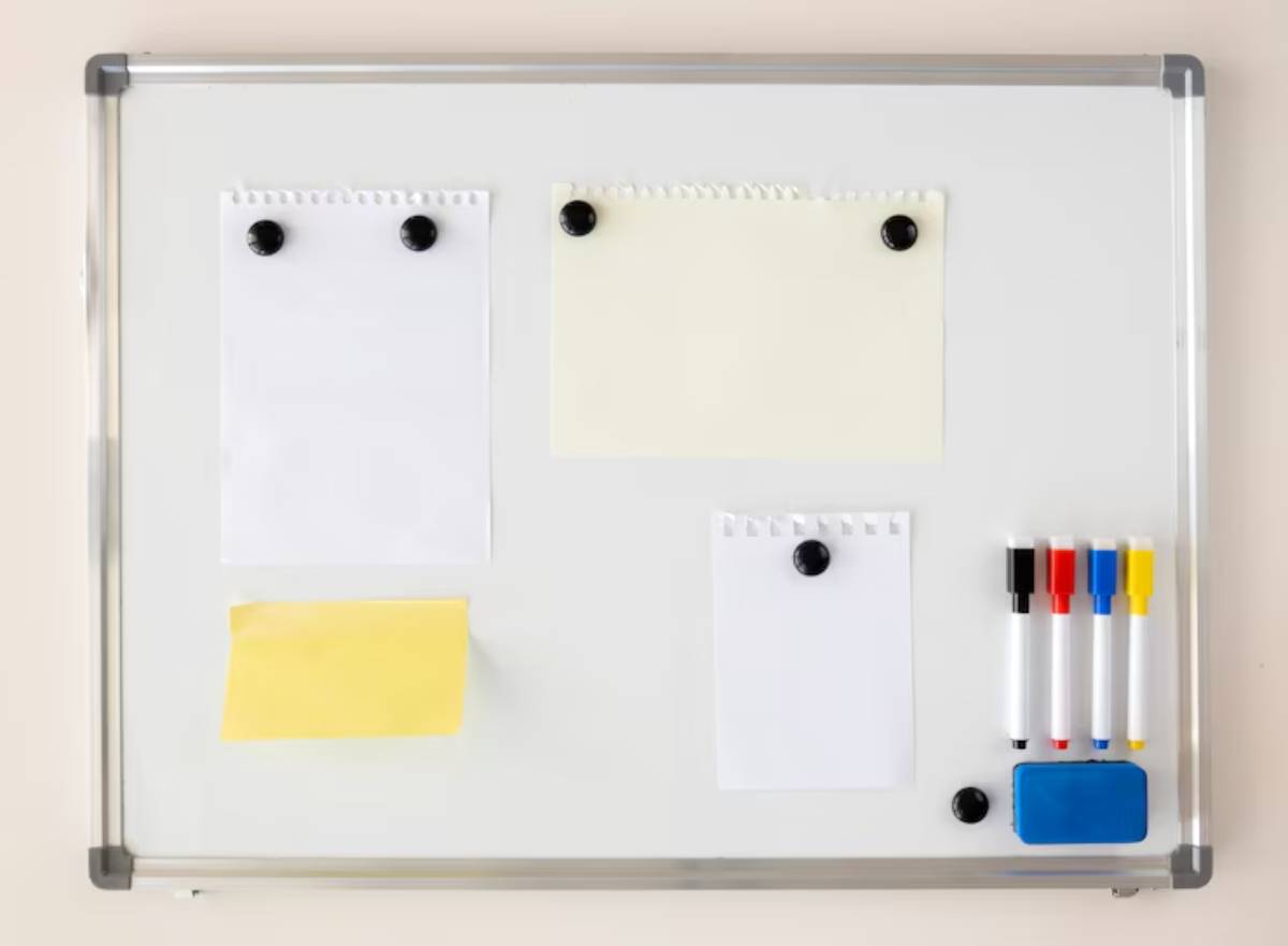 A whiteboard with assorted papers pinned on it, and colorful markers and an eraser neatly arranged on the side.