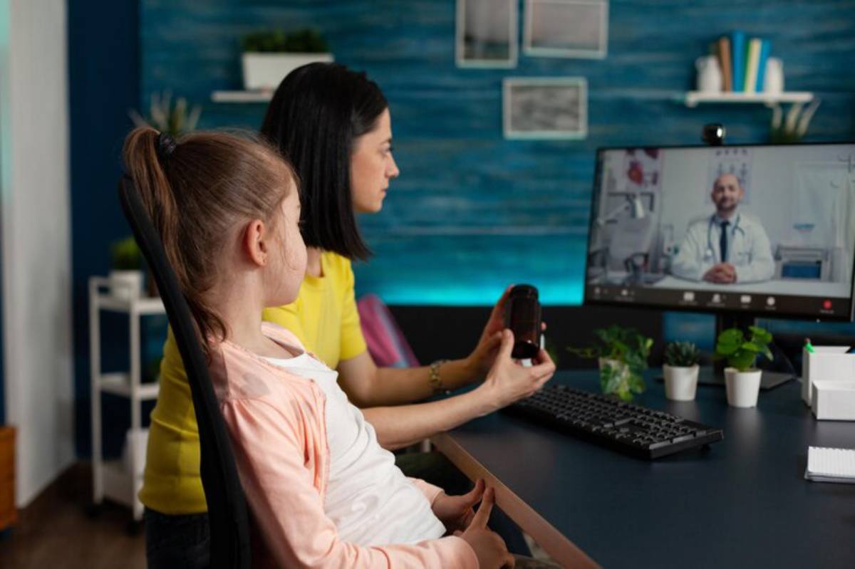  A laptop screen showing a speech therapist session with child-friendly visuals, and a parent assisting beside.