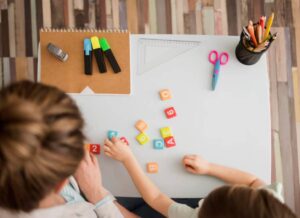A parent and child engage in playful learning with colorful number blocks on a table, surrounded by stationery and tools.